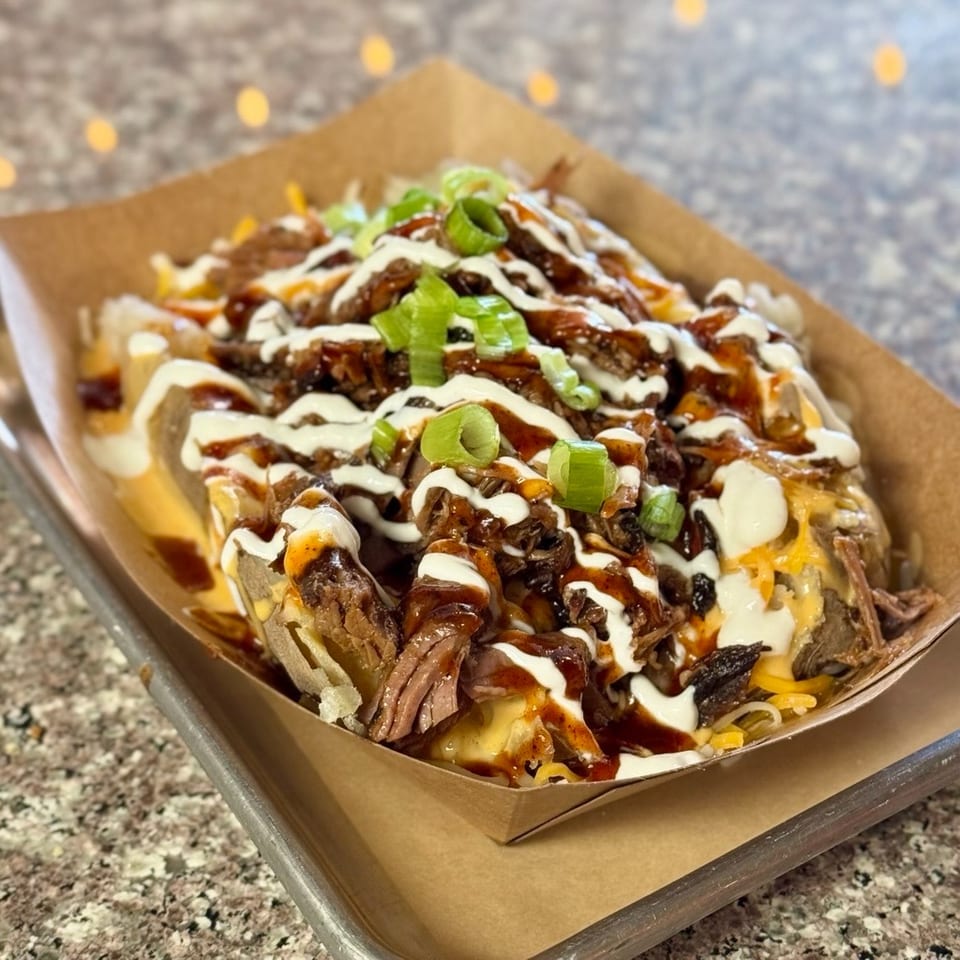 Loaded baked potato with pulled pork, cheese, sour cream, BBQ sauce, and green onions.