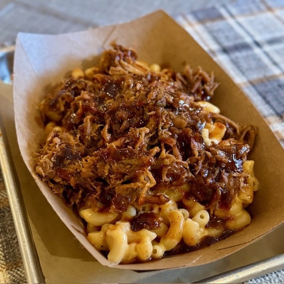 Pulled pork mac and cheese in a brown paper tray on a metal serving tray.