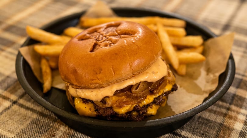 Cheeseburger with caramelized onions and special sauce, served with fries on a black plate.