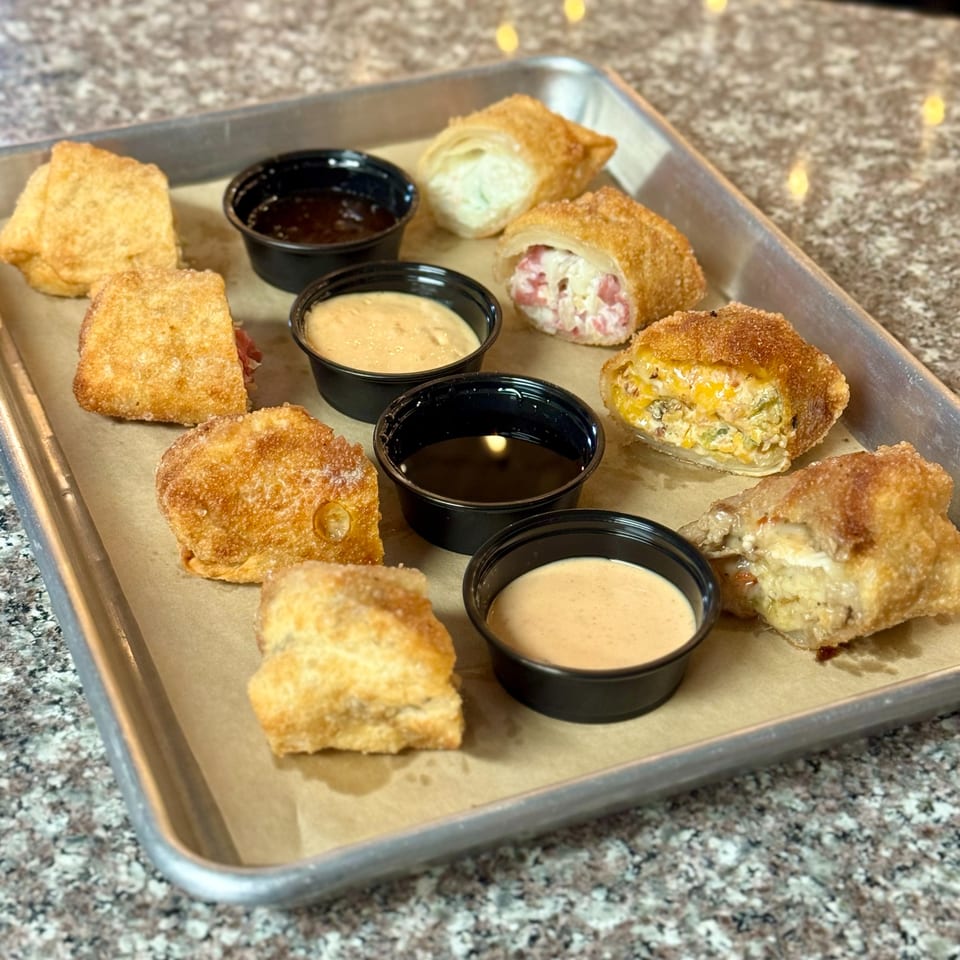 A metal tray with various fried appetizers and dipping sauces on a granite countertop.